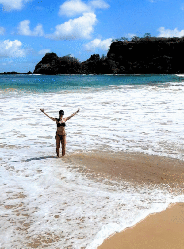 Mulher com os braços abertos dentro do mar em praia em Fernando de Noronha.