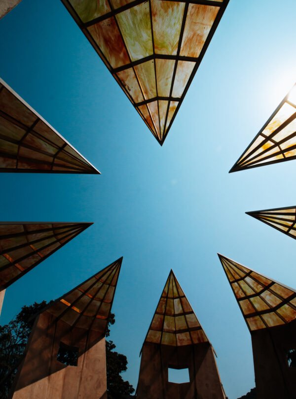 Fotografia de Bernardo Firme em ângulo contra-plongê (de baixo para cima), mostrando as pontas da estrutura metálica da obra de Robert Irwin no Instituto Inhotim. O teto vazado da instalação emoldura perfeitamente o céu azul intenso, destacando as linhas retas e o design minimalista.